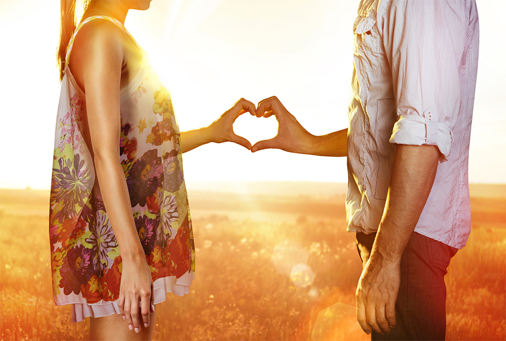 Couple in a field making a heart with their hands.