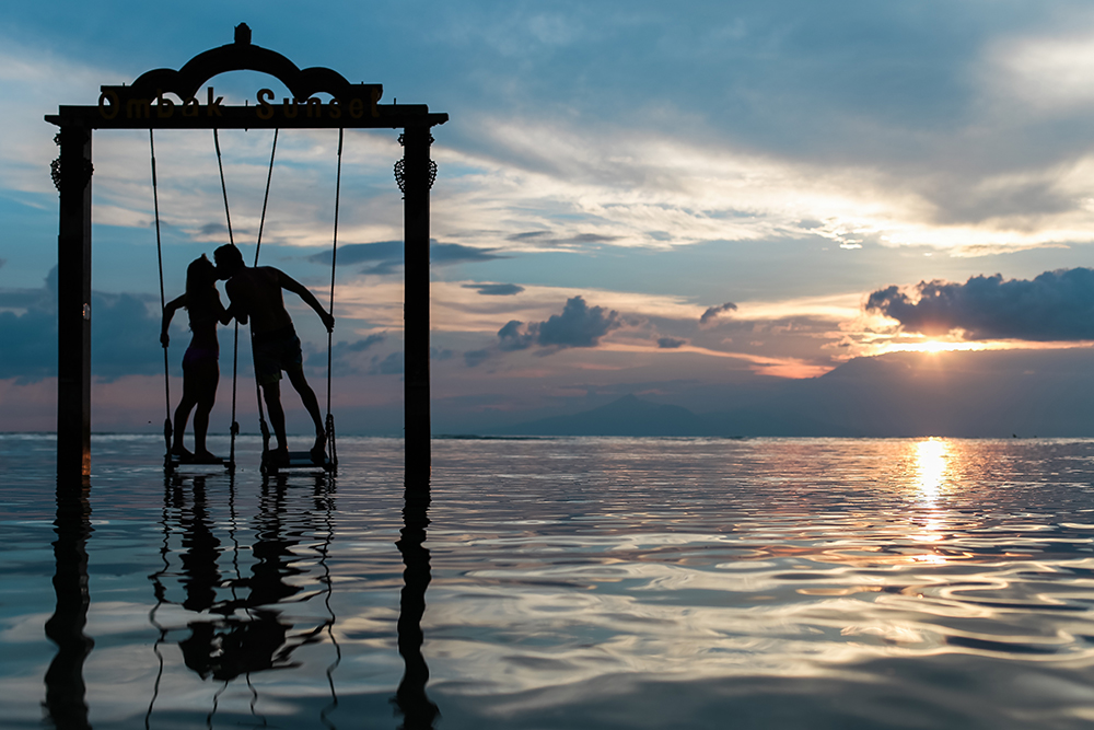 Couple kissing on swing in the ocean.