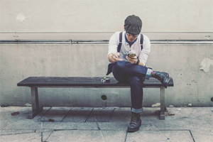 Man sitting on bench looking down at phone.