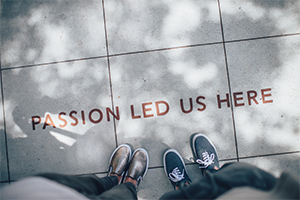 Two people standing in front of ground art that reads "PASSION LED US HERE."