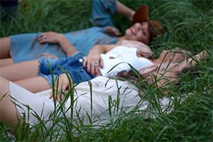 Three women laying in a grassy field together.