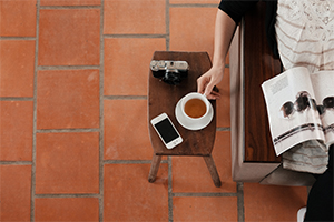 Woman reading magazine with her cell phone on a coffee table.