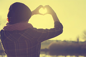 Woman looking into the distance making heart shape with her hands.