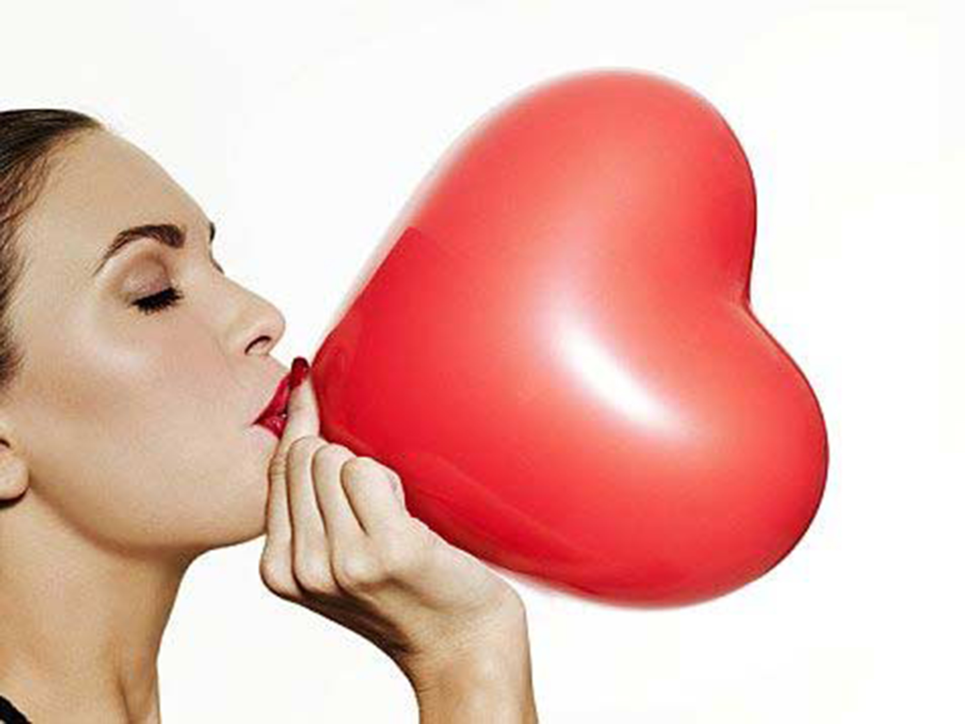 Woman blowing up a heart shaped balloon.