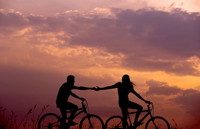 Couple holding hands biking in the sunset